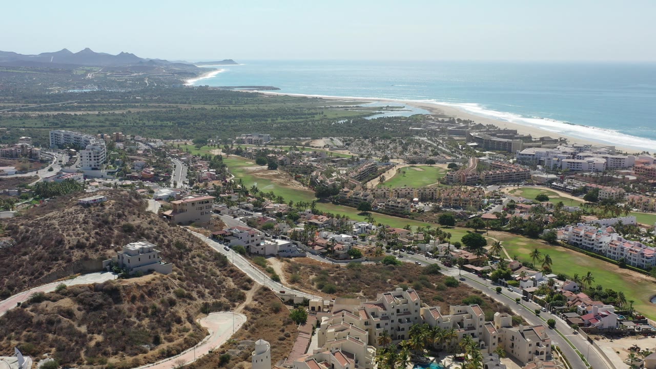 Aerial view over hillside homes, golf greens, coastline, and ocean.