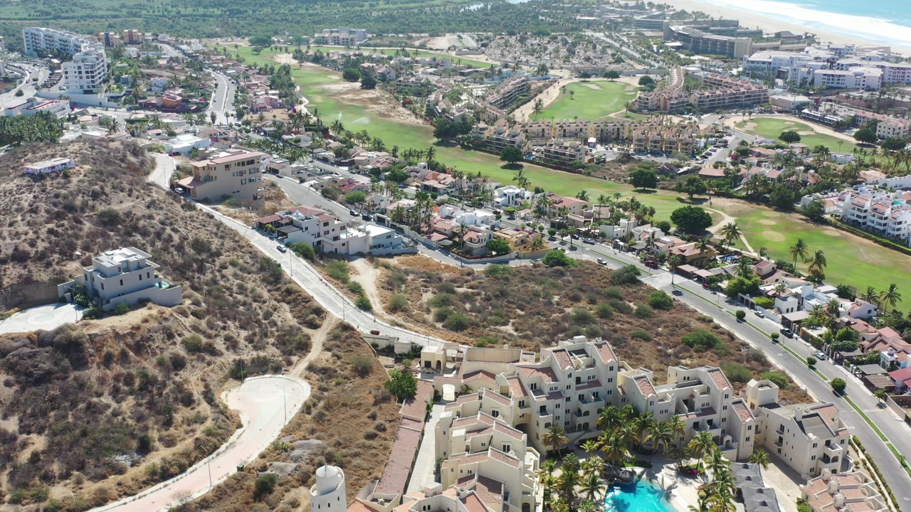 Aerial view of hillside homes, roads, golf greens, and distant ocean.