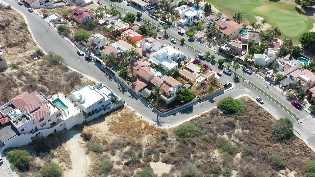 Aerial view of houses, roads, dry lots, and a green landscaped area.