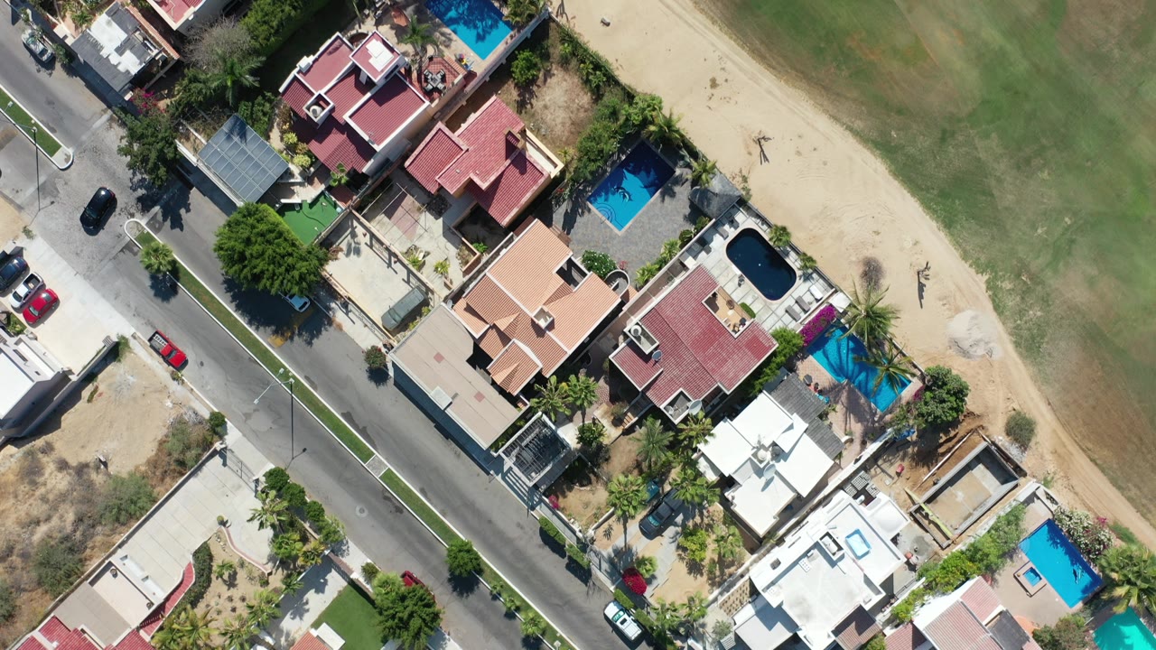 Top-down aerial view of homes, pools, road, and green field.