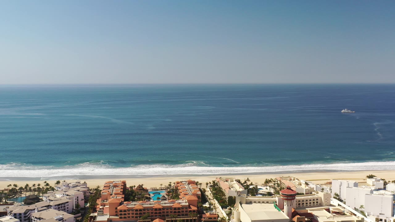 Aerial coastline view with ocean horizon, surf, beach, and clustered buildings.