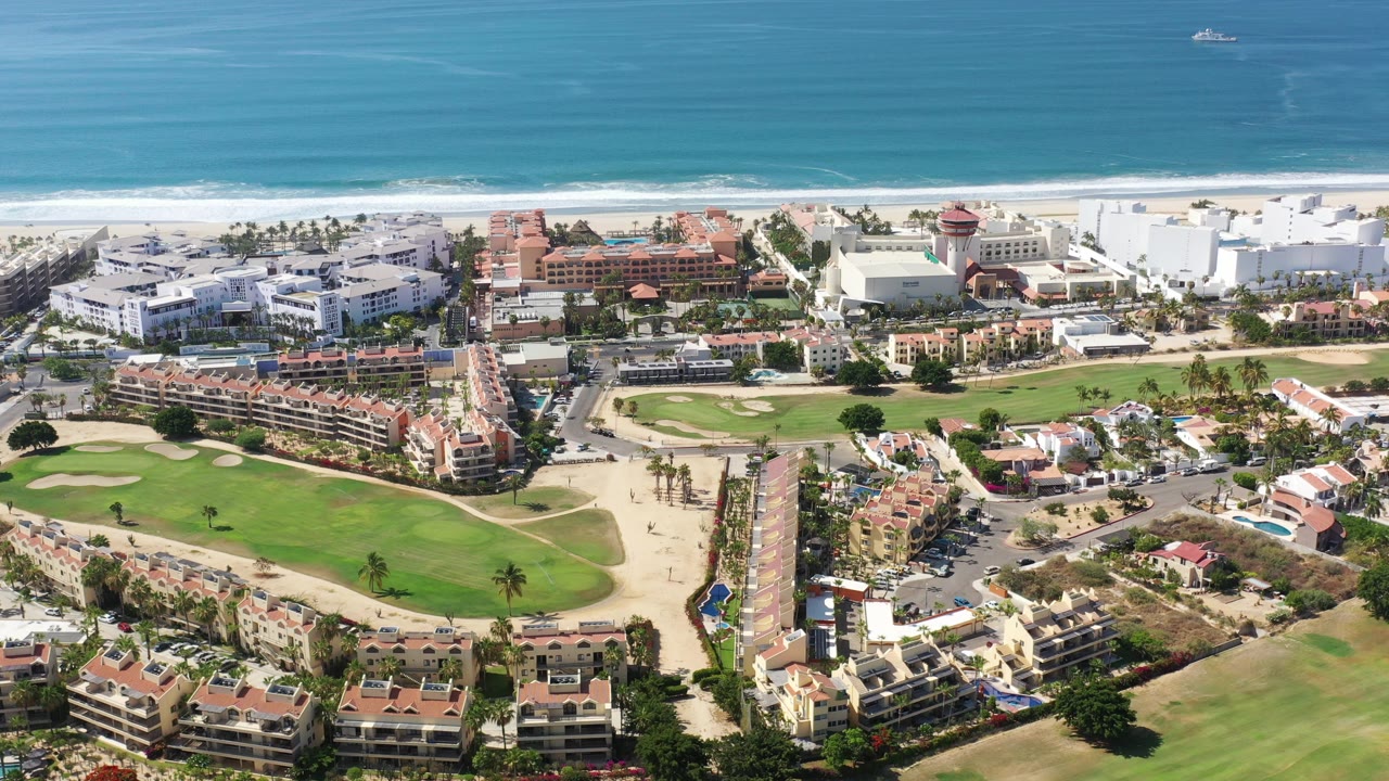 Aerial view of golf fairways, resort buildings, beach, and blue sea.