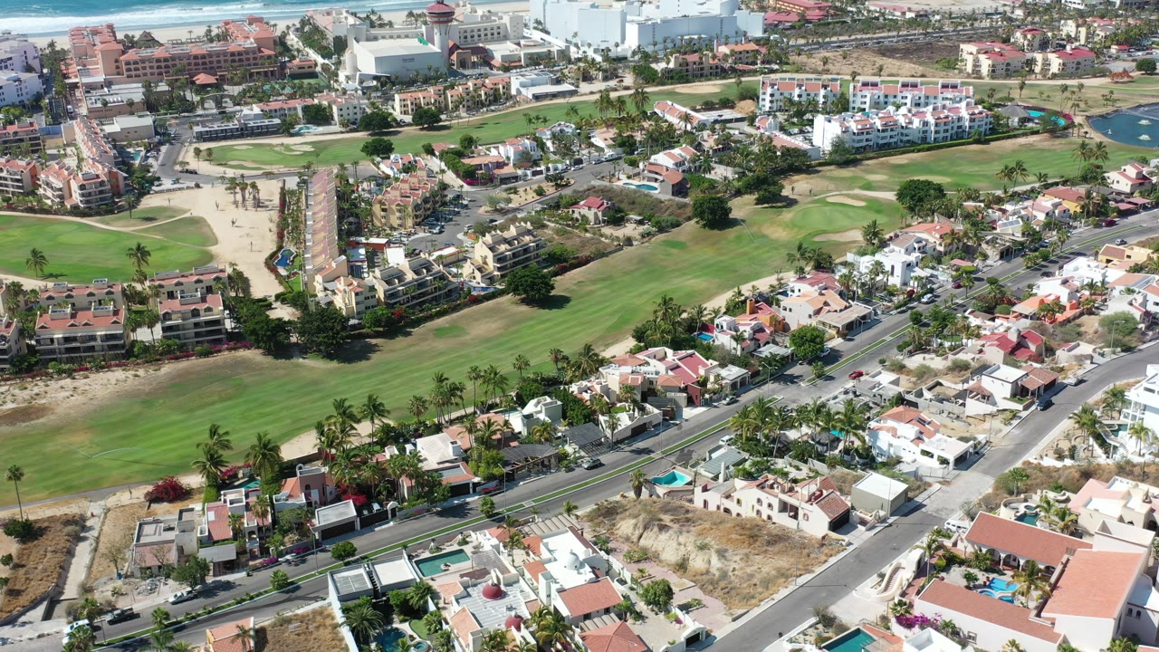 Aerial view over green lawns, roads, homes, and coastal buildings.