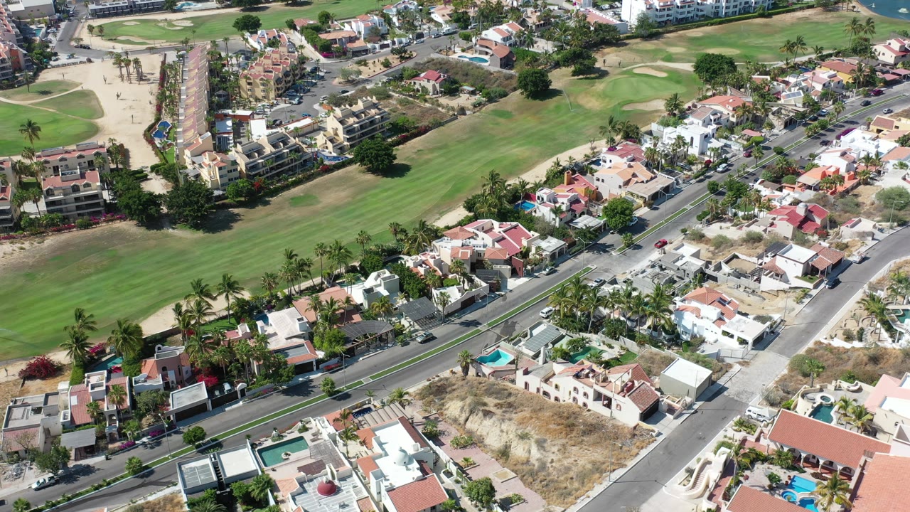 Drone-style view of rooftops, streets, pools, and a golf-like green area.