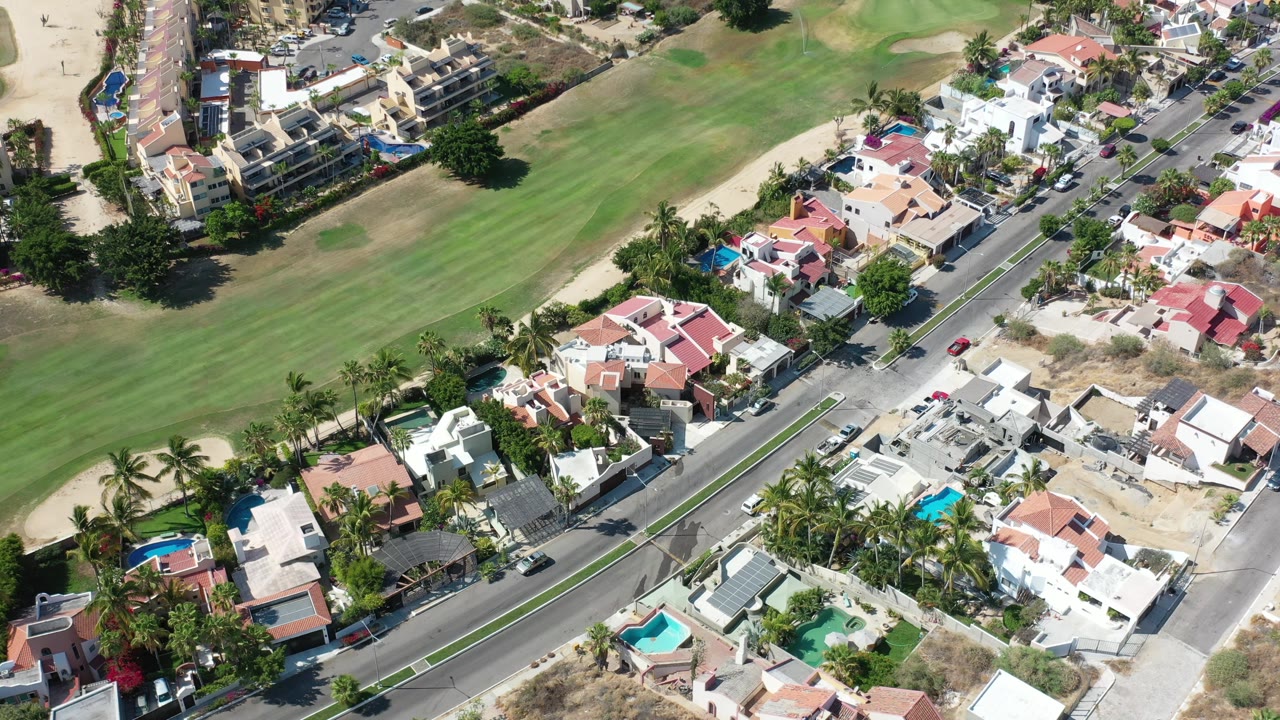 Drone-like overhead angle on homes, pools, street traffic, and a green landscaped course.