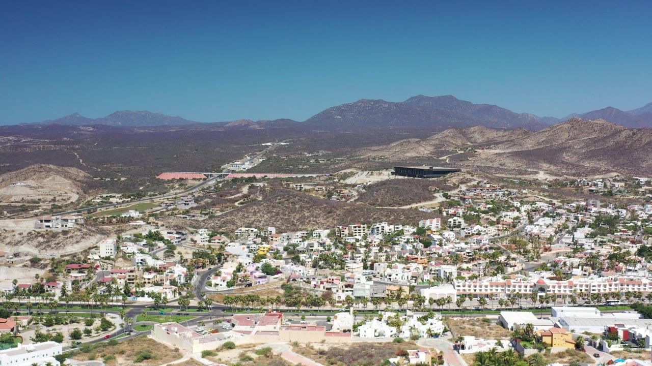Aerial view of a sunlit city below dry hills and distant mountains.