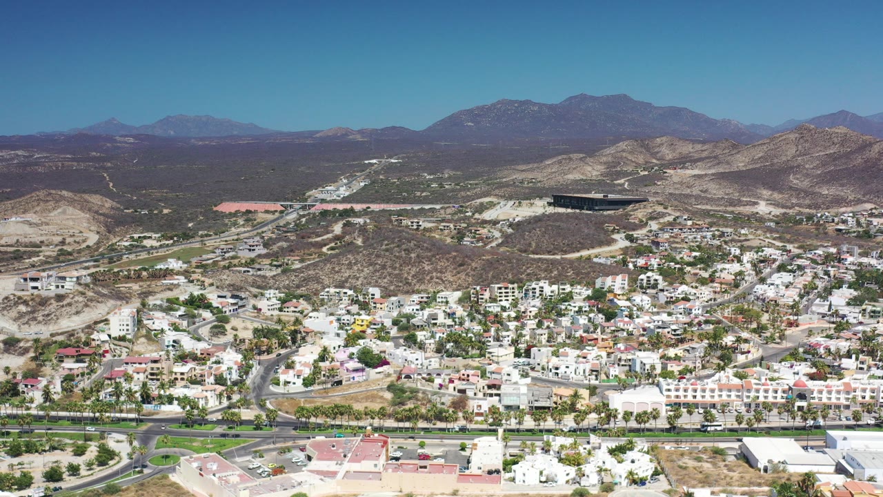 Aerial view of white houses, roads, dry hills, and distant mountains.