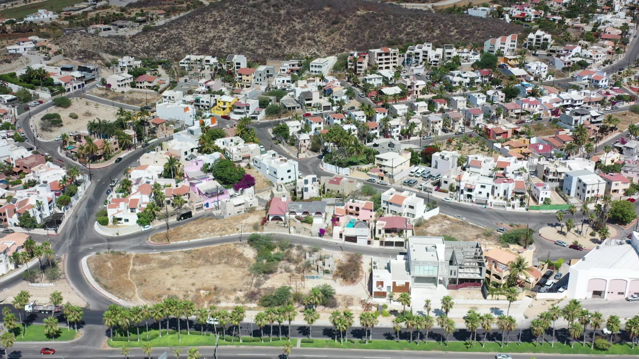 Aerial view of curved streets, homes, palms, and dry lots.