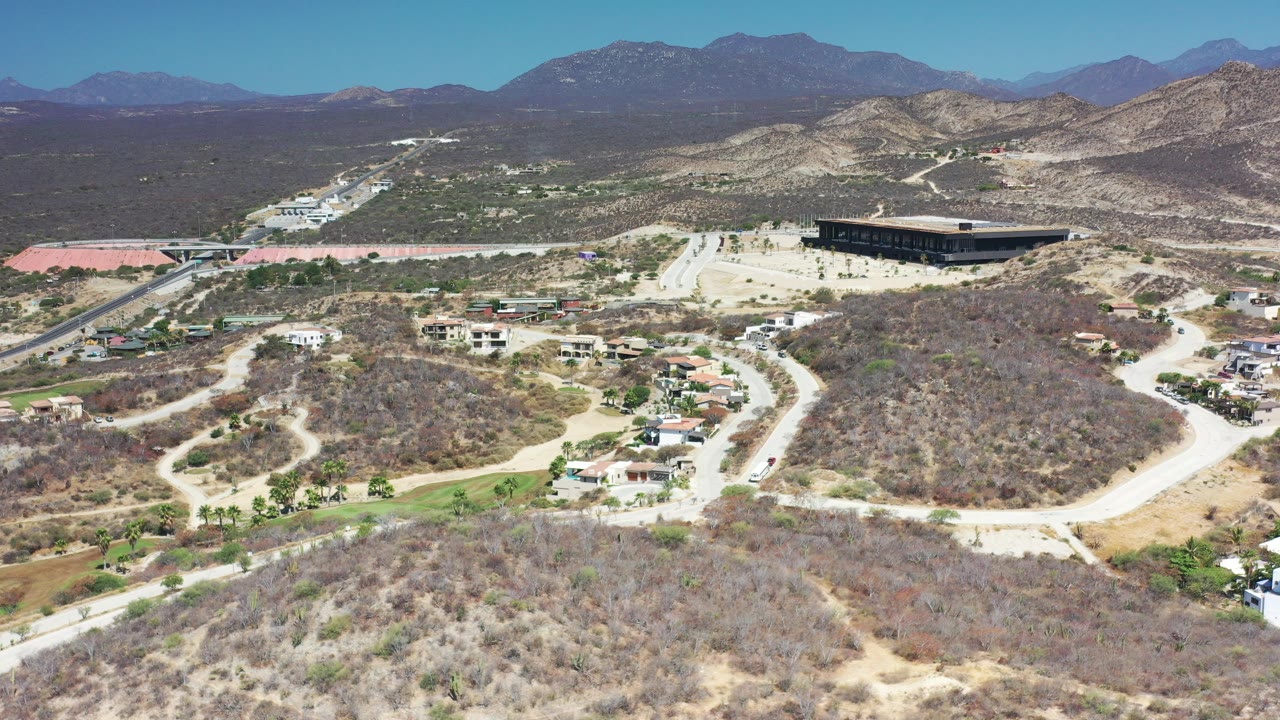Aerial view of dry hills, roads, homes, and distant mountains.