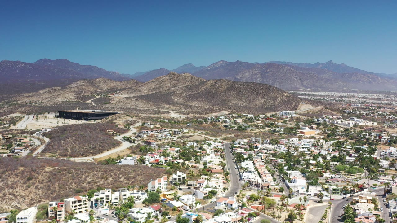 Aerial view over residential streets, dry hills, and distant mountains.