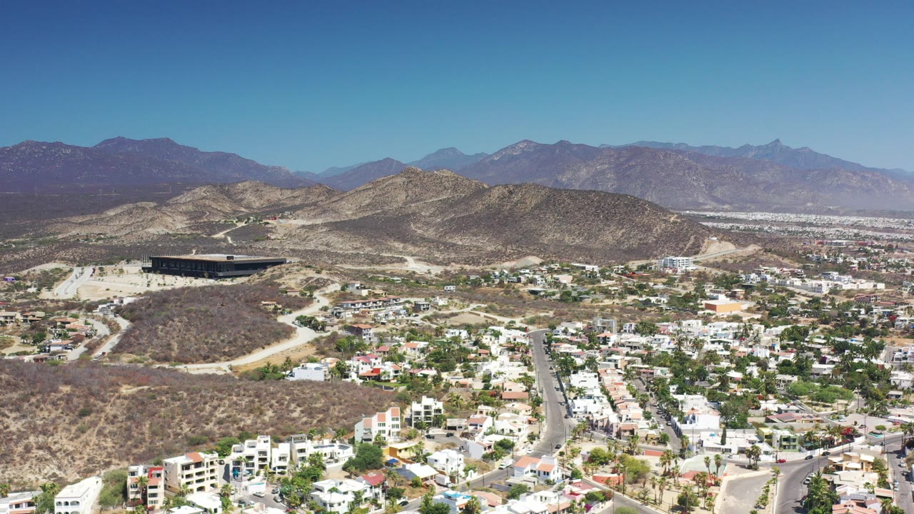 High aerial view of hillside homes, roads, dry hills, mountains, and blue sky.
