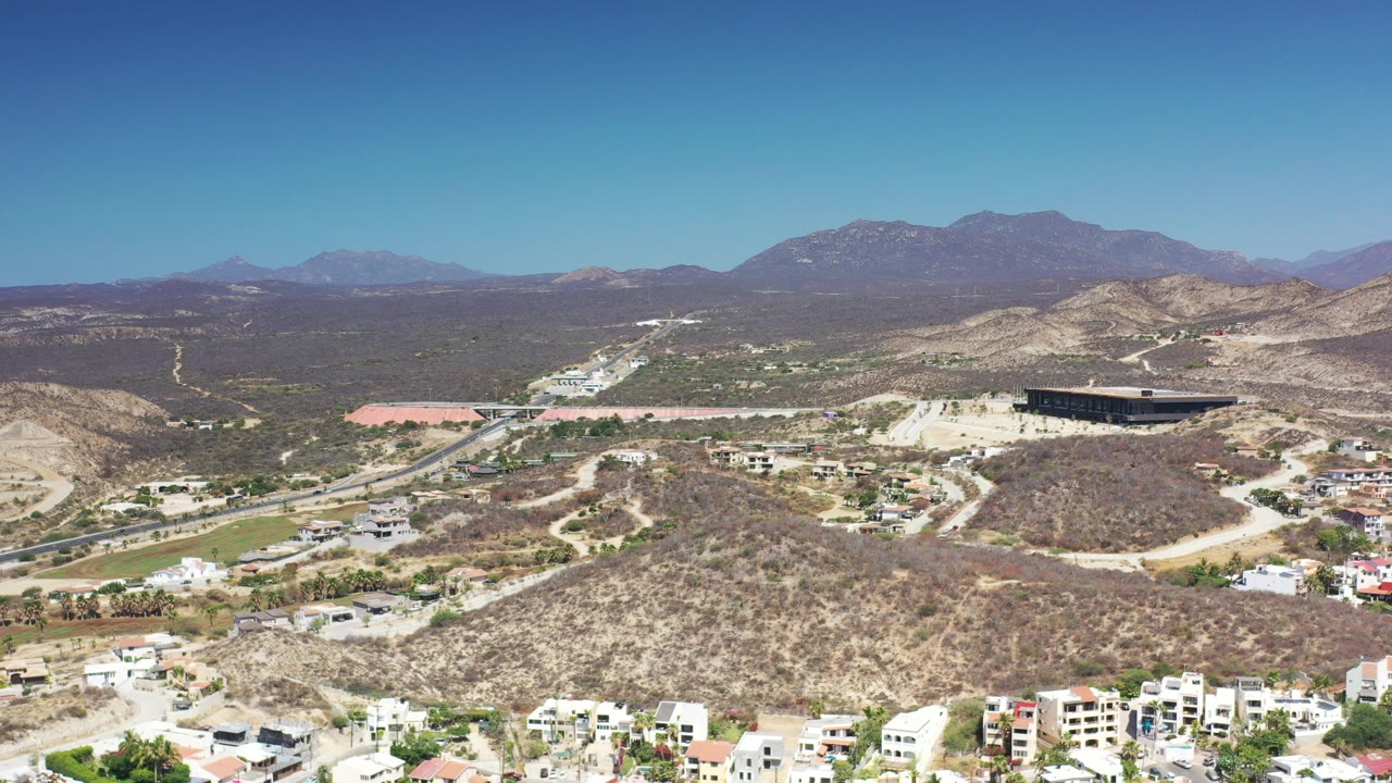 Aerial view of desert hillside homes, a road, and mountains in bright daylight.