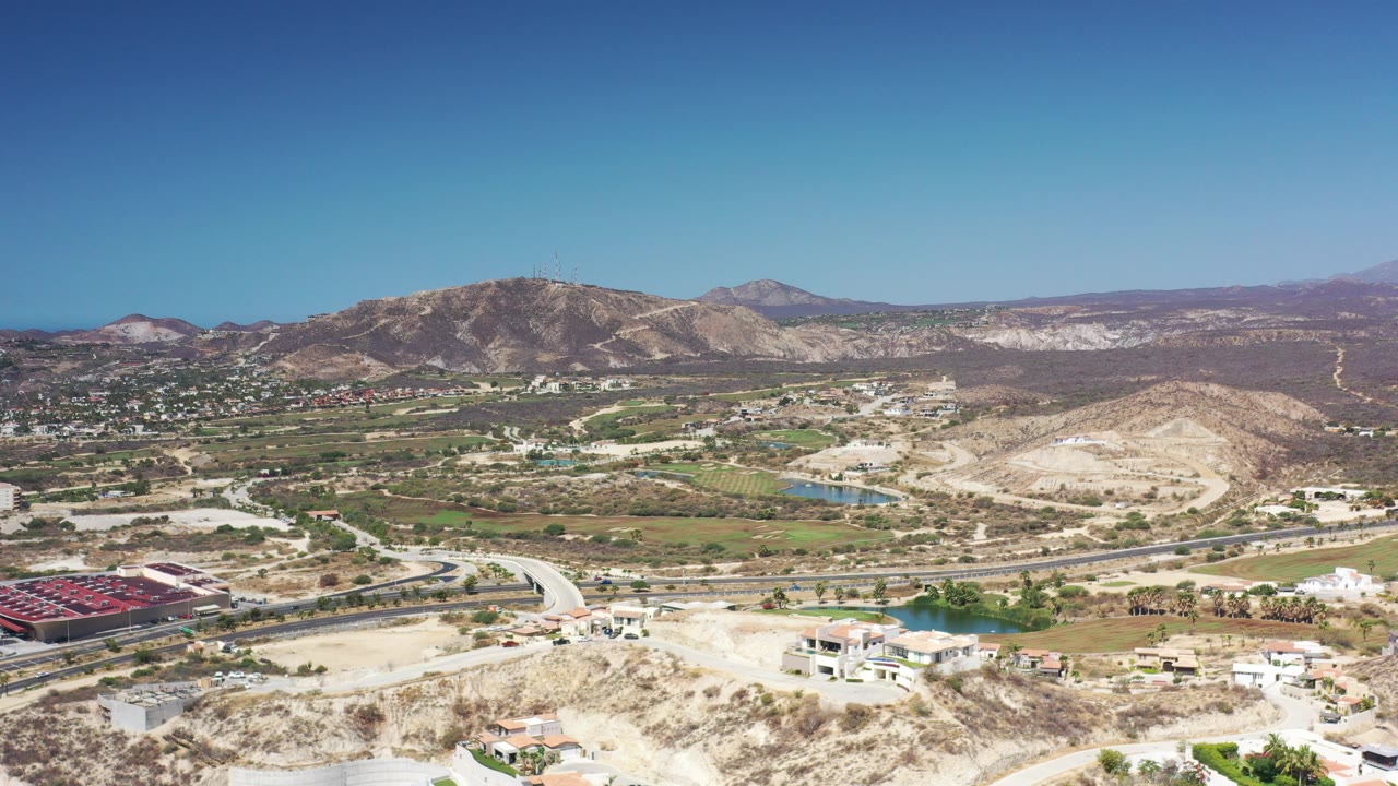 Aerial view of rural roads, hills, buildings, and mountains under blue sky.