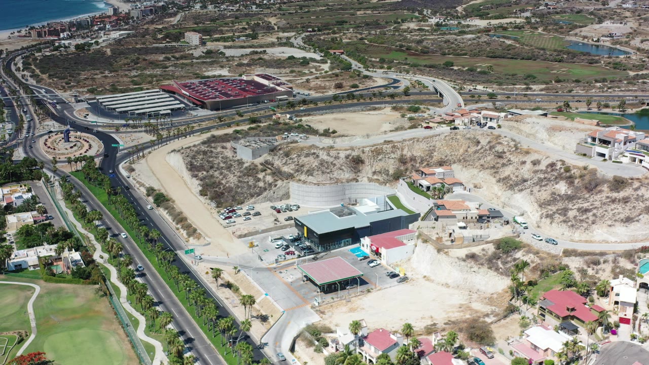 Aerial view of a road, roundabout, hillside lots, and low buildings.