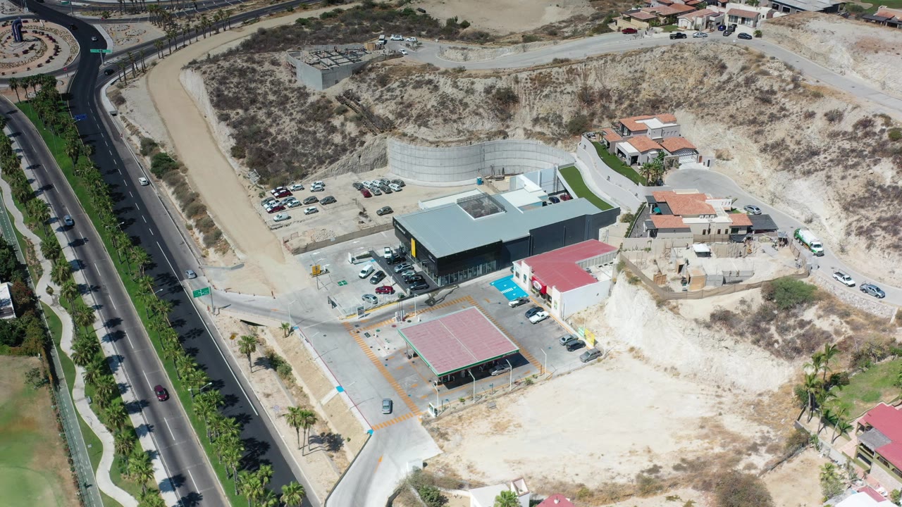 Aerial view of modern buildings, parking areas, roads, and dry hillside terrain.