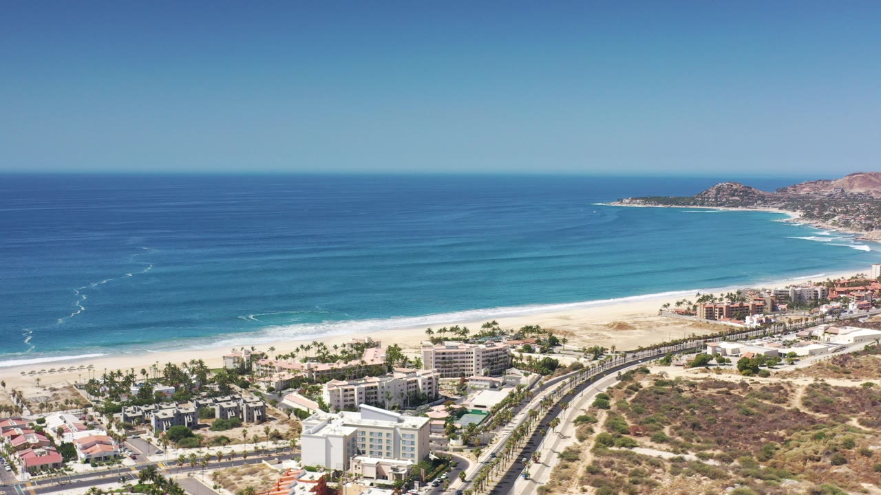 Aerial view of beach, ocean, buildings, and road under clear sky.