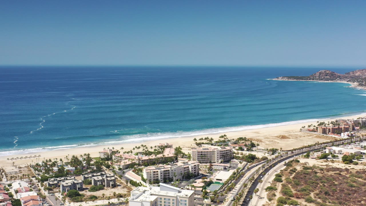 Aerial view of beachfront hotels beside white sand and turquoise sea.