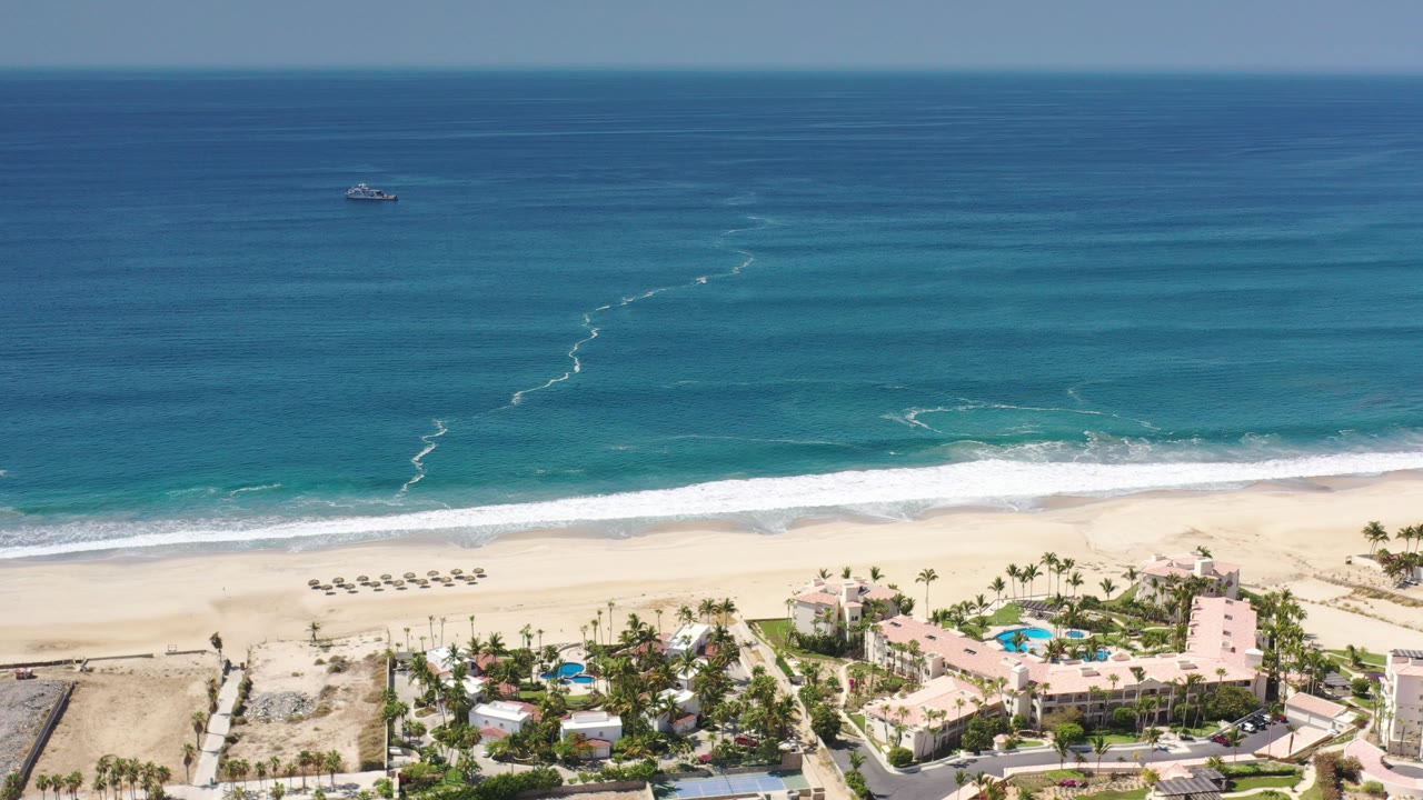 Aerial view of ocean, beach, resort buildings, pools, and umbrellas.