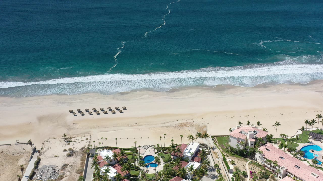 Aerial view of surf, sand, beach umbrellas, and coastal homes.