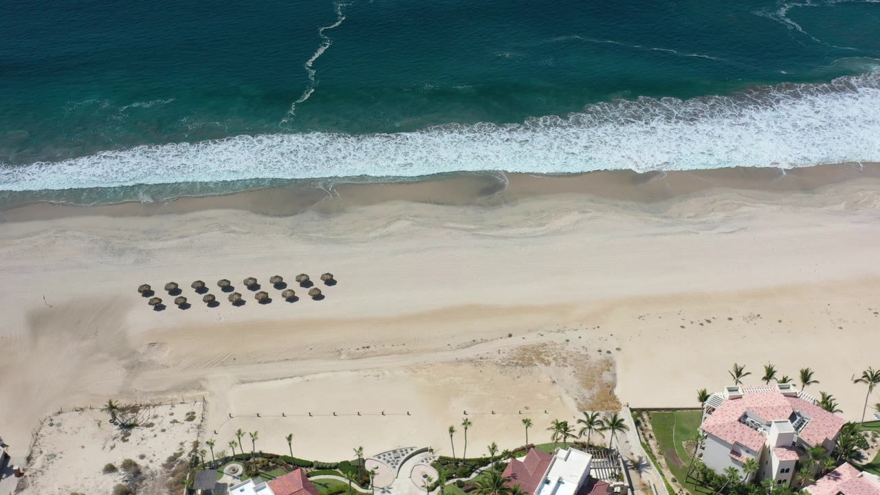 Overhead beach with surf, sand, umbrellas, and rooftops