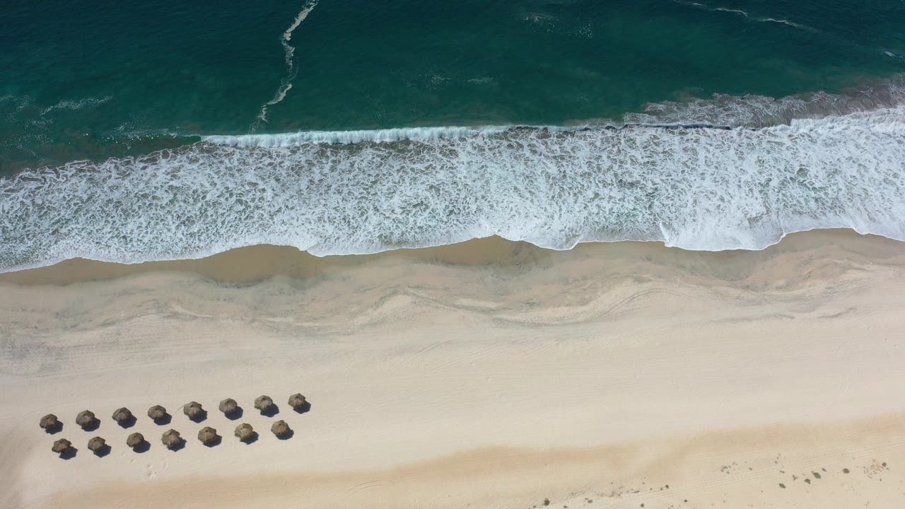 Overhead surf line, sandy beach, and rows of beach umbrellas.