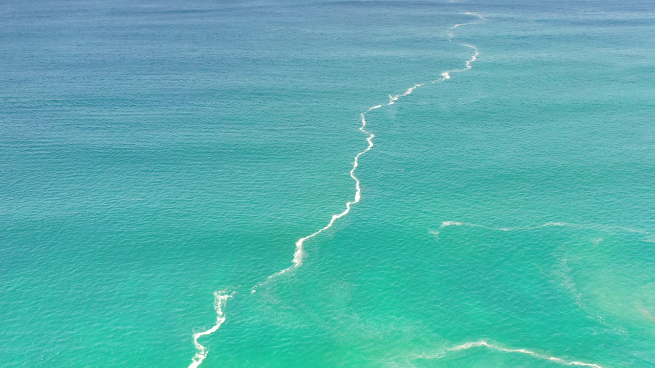 Elevated view of blue-green ocean water in Los Cabos, Mexico, with a narrow white surf line crossing the frame and no visible people.