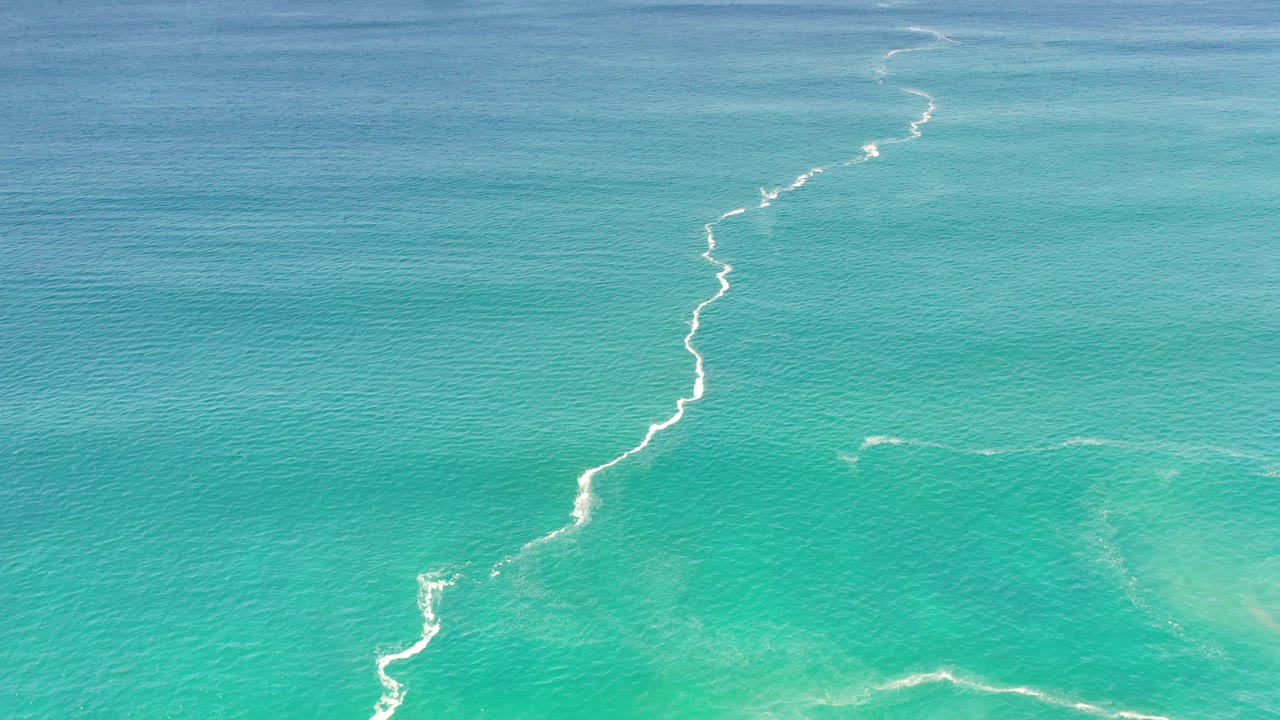 Turquoise Los Cabos ocean water fills the frame, with pale breaking water running vertically through the center and no visible people.