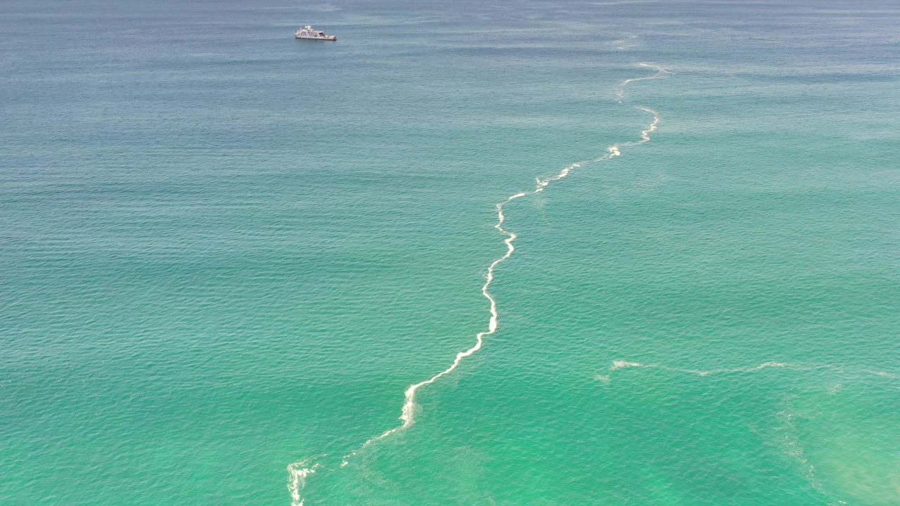 Ocean surface with white water trail and distant boat