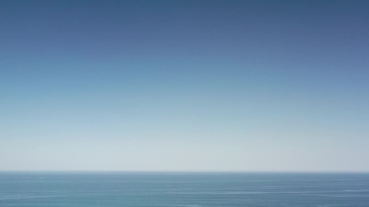 A small distant boat appears offshore in the Los Cabos water, with a pale blue sky and no visible people.