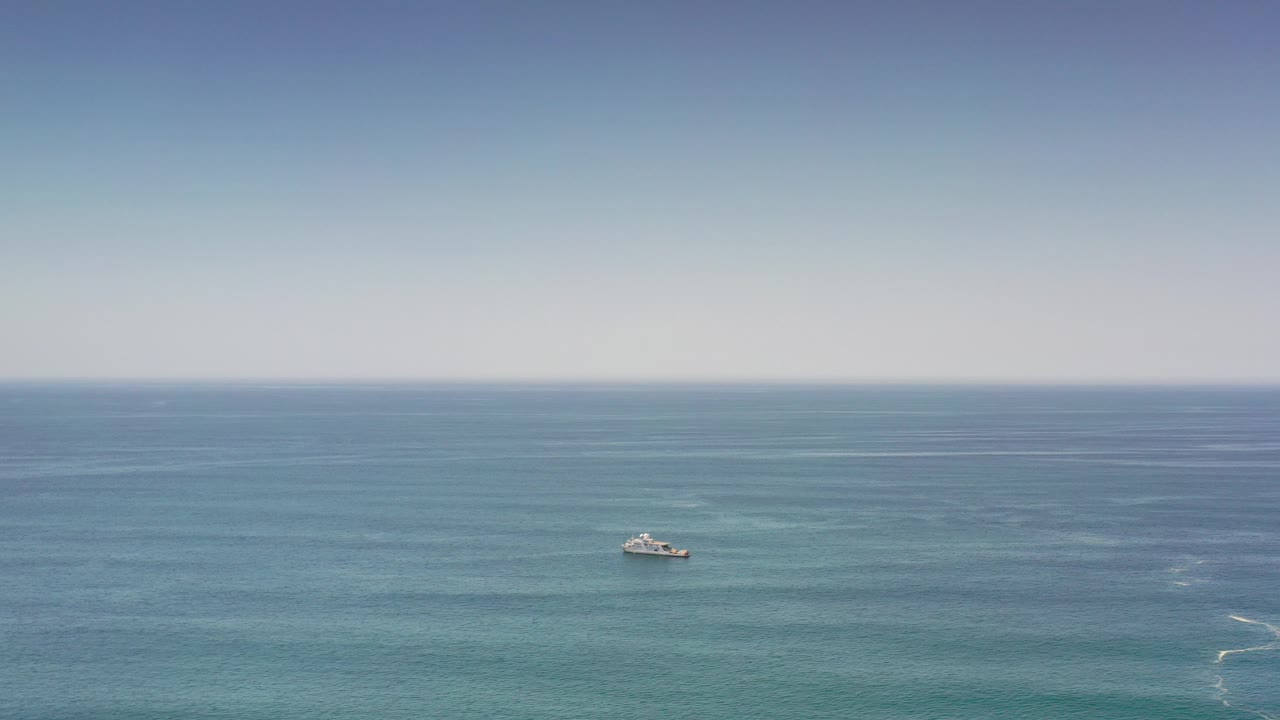Wide Los Cabos ocean view with a small gray-white ship left of center on green-blue water, pale sky above, and no visible people.
