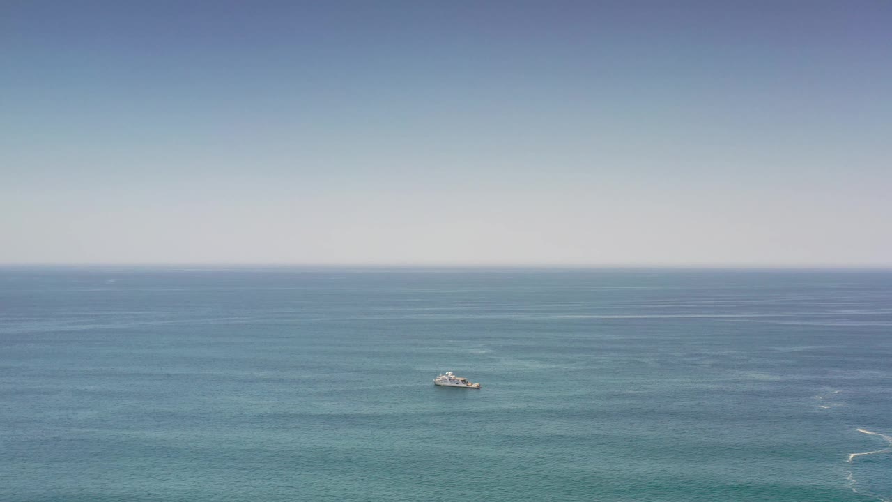 Wide Los Cabos sea frame with the ship near the center, turquoise water patterns below it, a flat horizon, and no visible people.