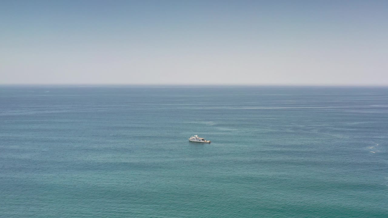 Boat at sea with turquoise water bands beneath a clear horizon.