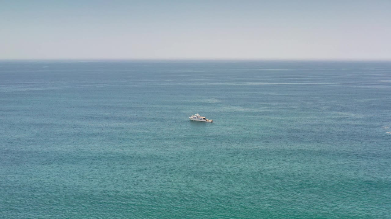Wide aerial-style view of Los Cabos water with the small boat near the center, soft wave bands across the sea, and no visible people.
