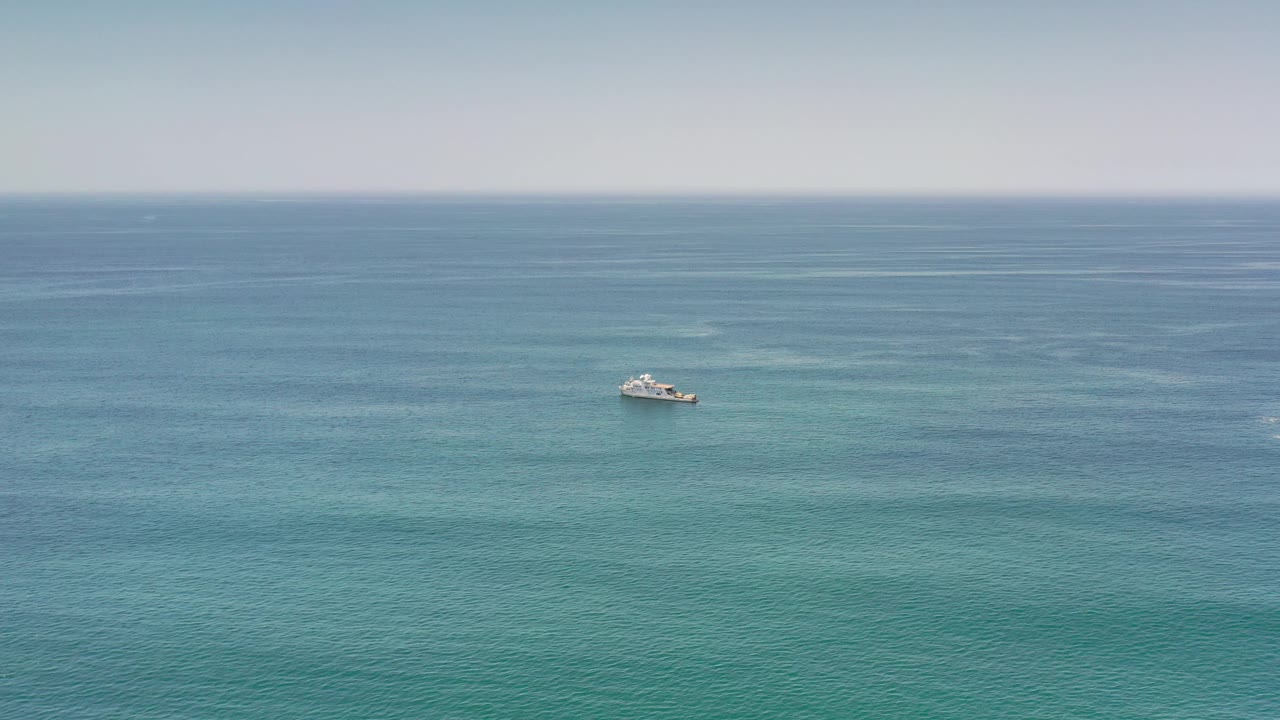 Single boat farther right on calm ocean under hazy sky.