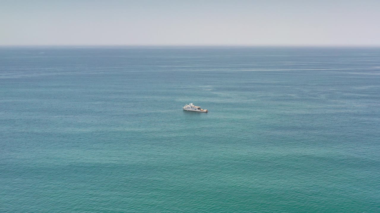 At 0:00, a small white boat appears far out on blue and turquoise ocean water near Los Cabos, Mexico, with a pale horizon and no visible people.
