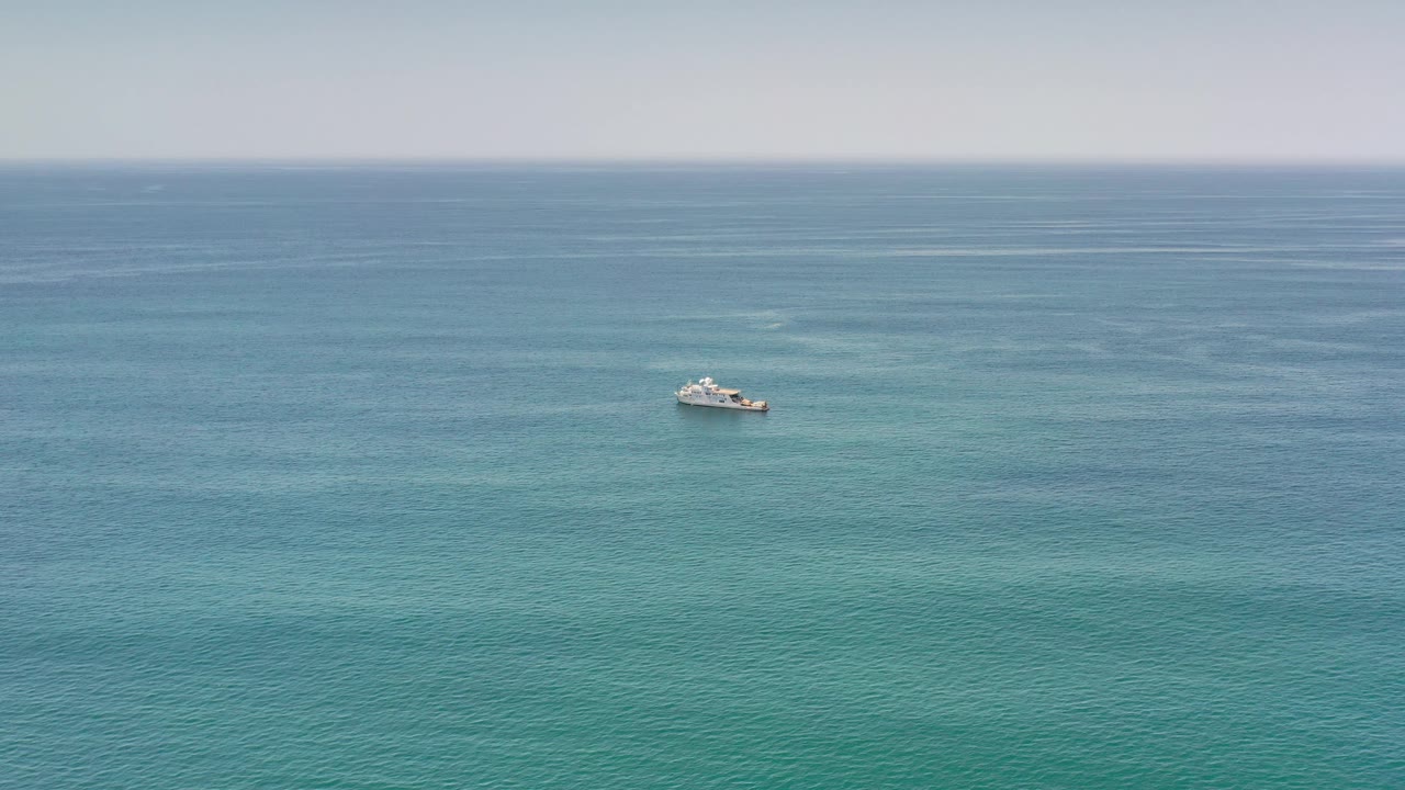 White boat far offshore on blue-green ocean water.