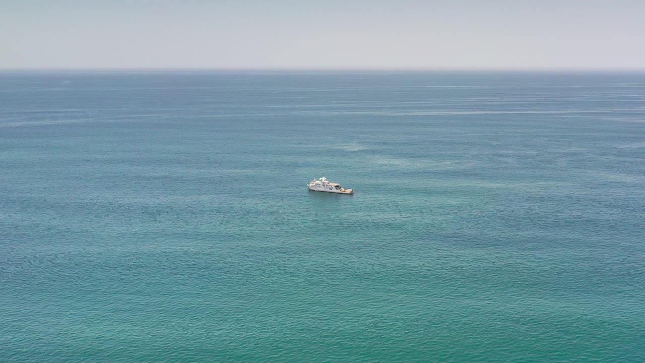 Wide Los Cabos, Mexico ocean view with a small white boat left of center, rippled blue-green water, a hazy horizon, and no visible people.