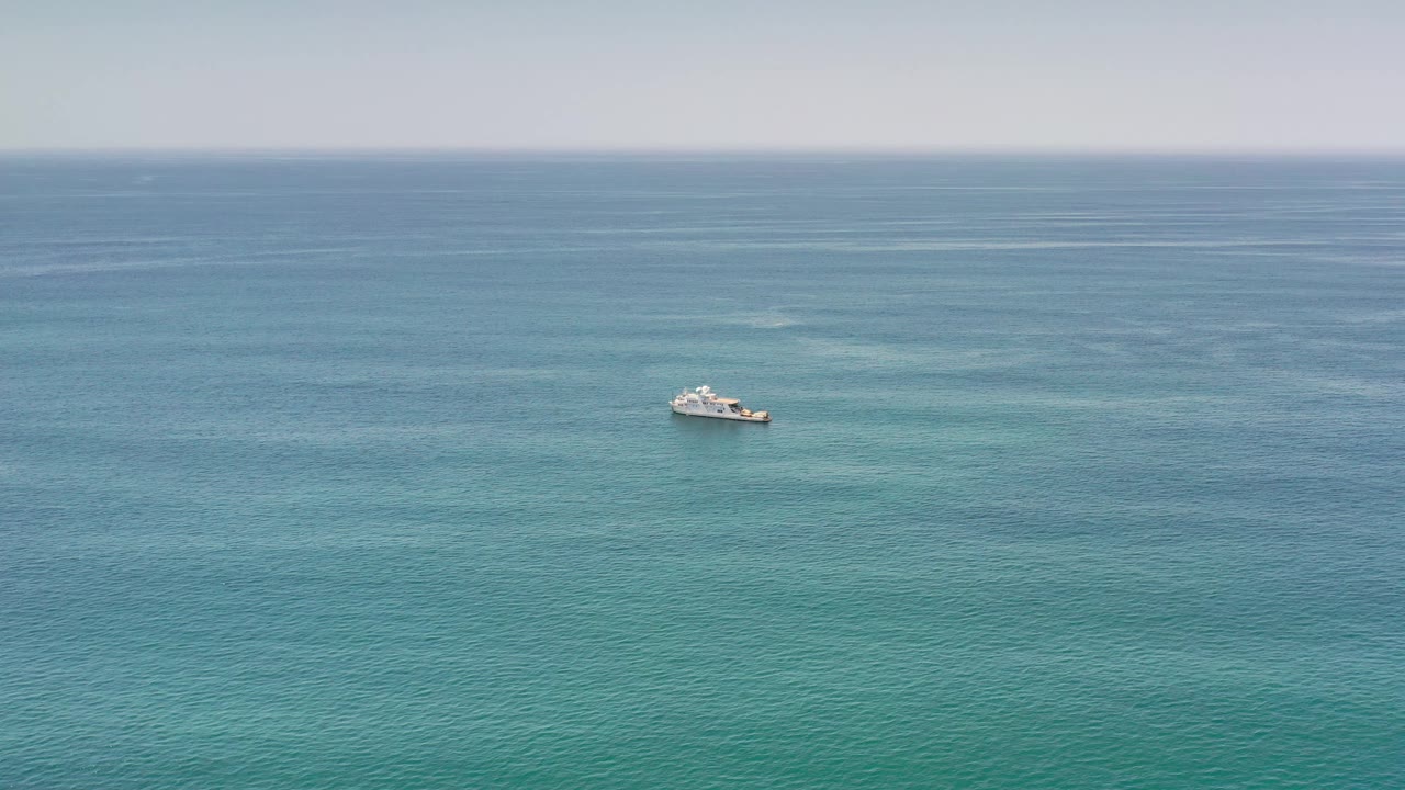 Distant white boat crossing open turquoise water.