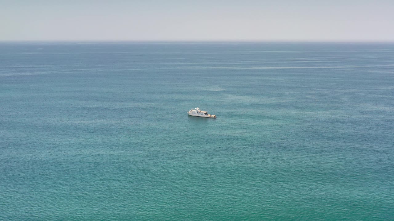Wide coastal water view in Los Cabos with a small white boat toward the right, blue sea stretching to a soft horizon, and no visible people.