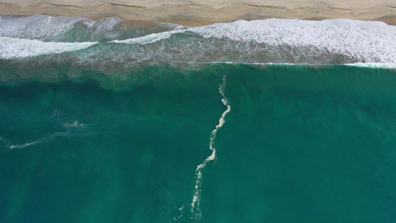 Overhead turquoise ocean water and white surf along sand.