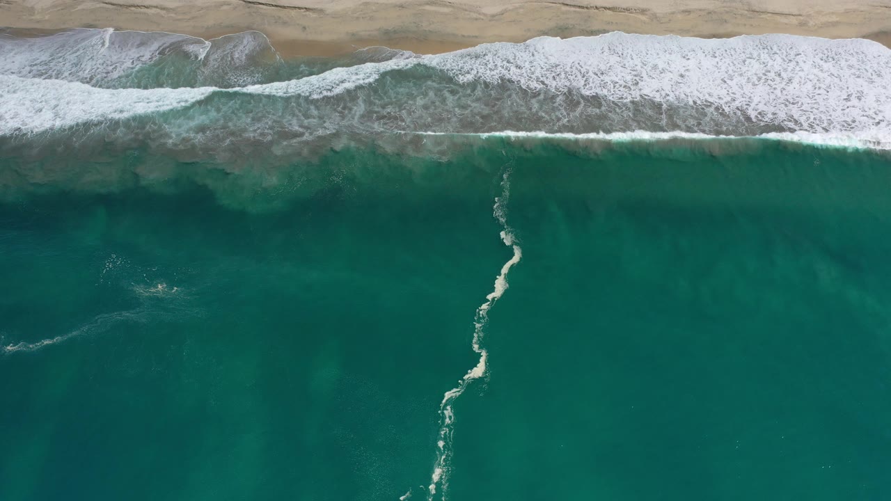 Foam trail divides turquoise water below a breaking wave.