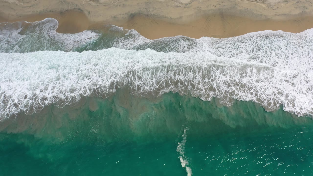 Breaking wave washing toward sandy beach from above