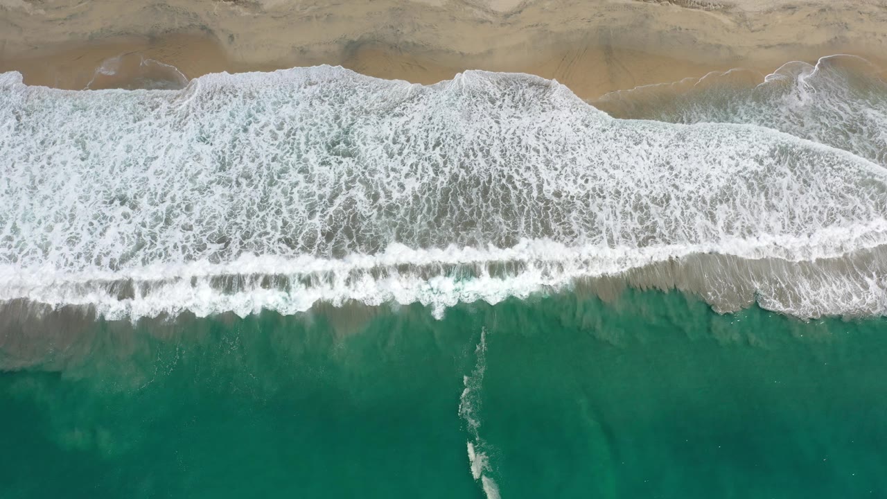 Wave foam crossing a tan sand shoreline