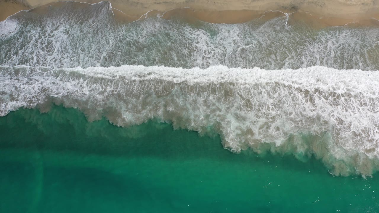 Foamy surf spreads across shallow water near a sandy shore.