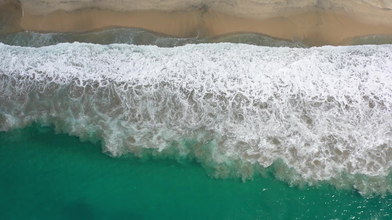 Aerial beach frame with thick white surf and turquoise water.