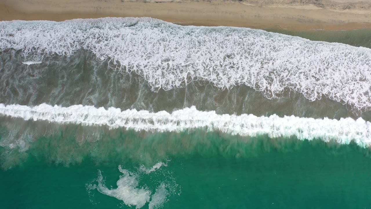 Aerial surf pattern over green water and tan sand