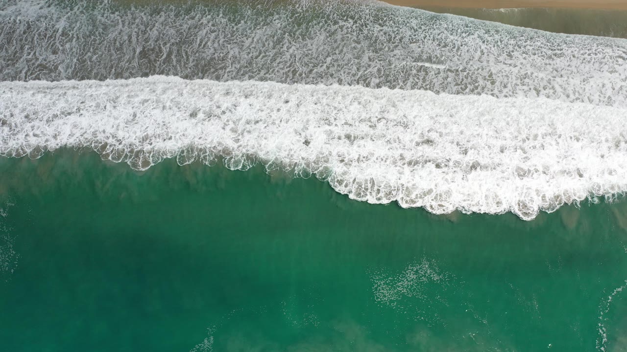 Foam band curls over green ocean with sand visible at the top.