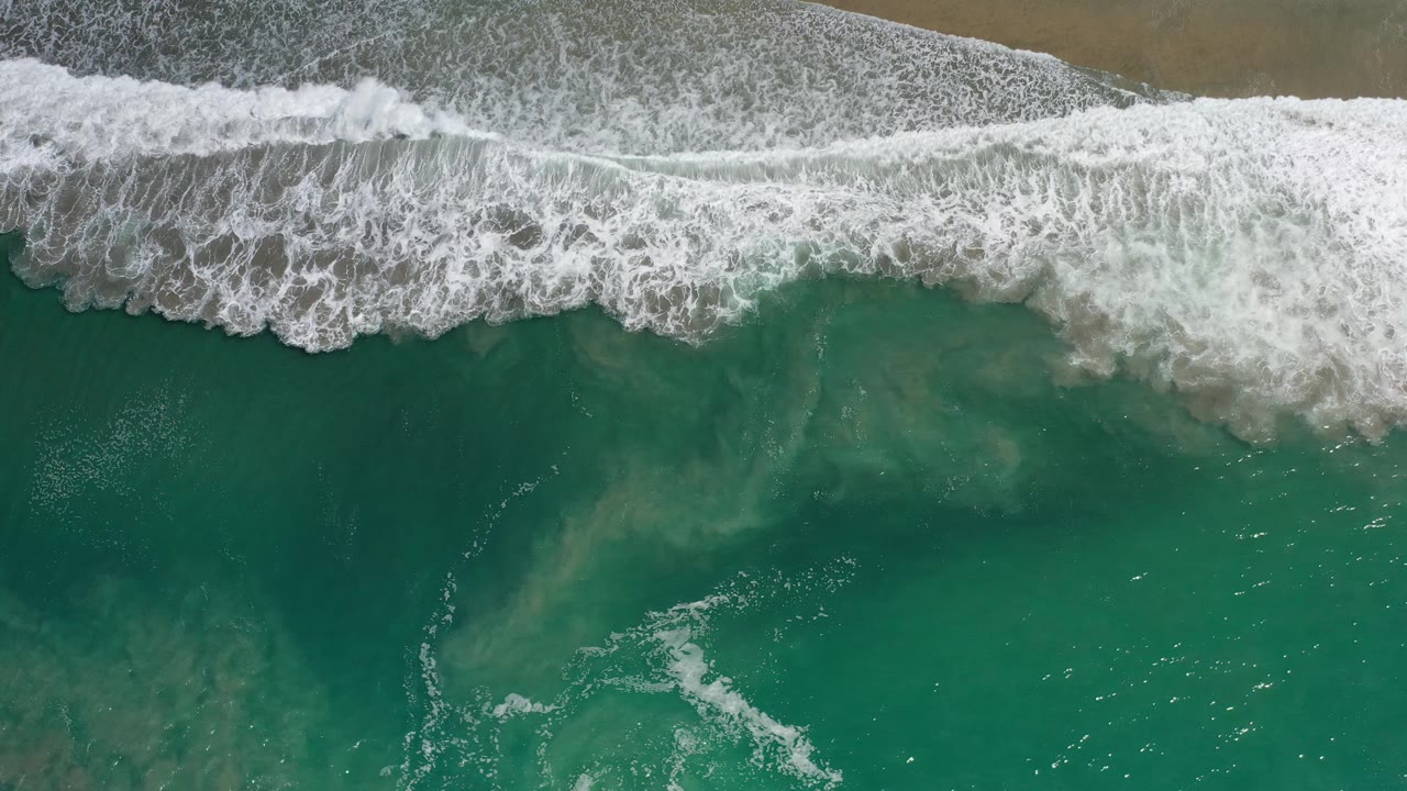 Aerial view of foamy waves and clear teal ocean