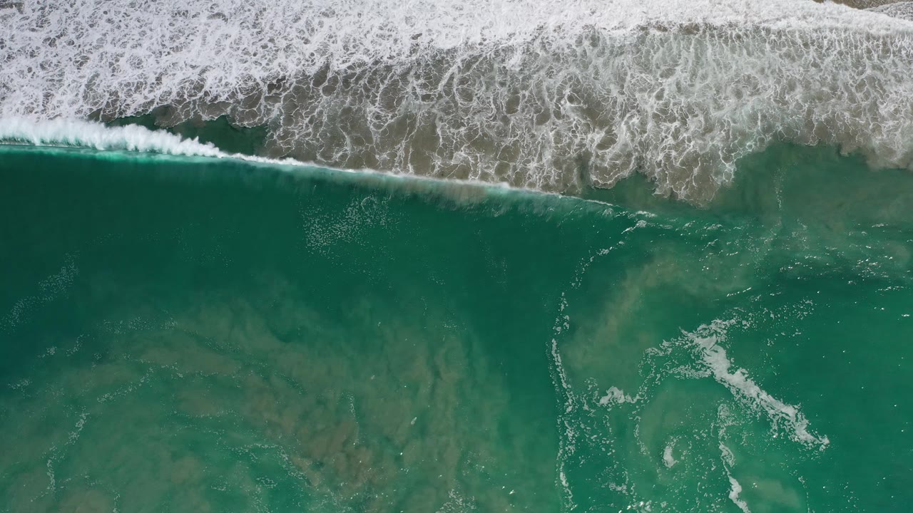 Top-down green ocean with a long white breaking wave at the top.