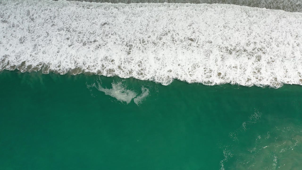 Overhead view of green ocean water in Los Cabos, Mexico, with a thick band of white surf breaking across the top and no visible people.